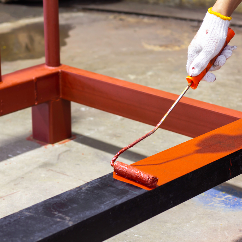 Worker painting a wooden structure with orange paint.